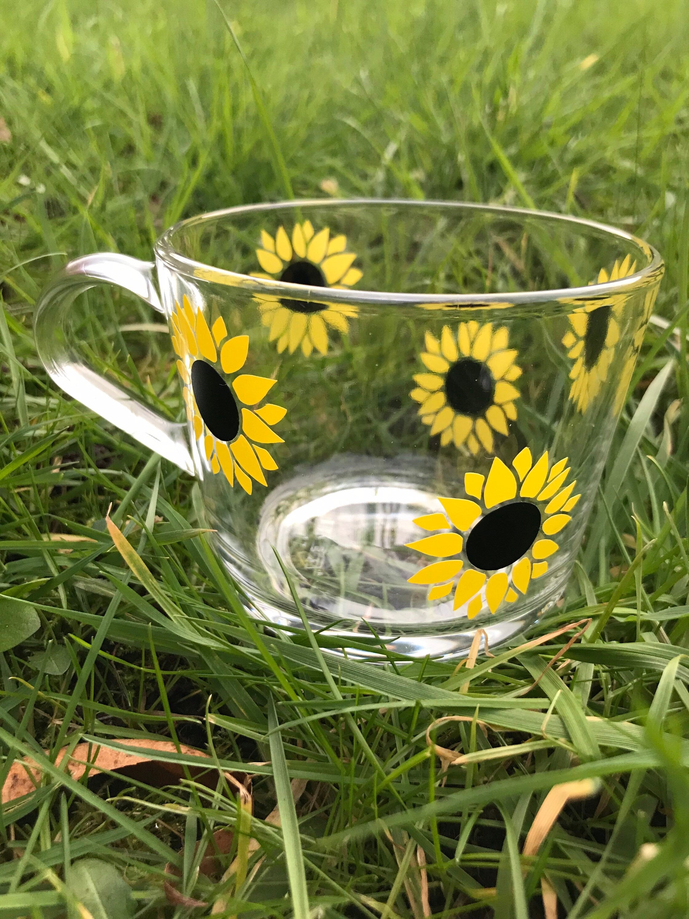 Clear glass mug with sunflower designs on a grass background
