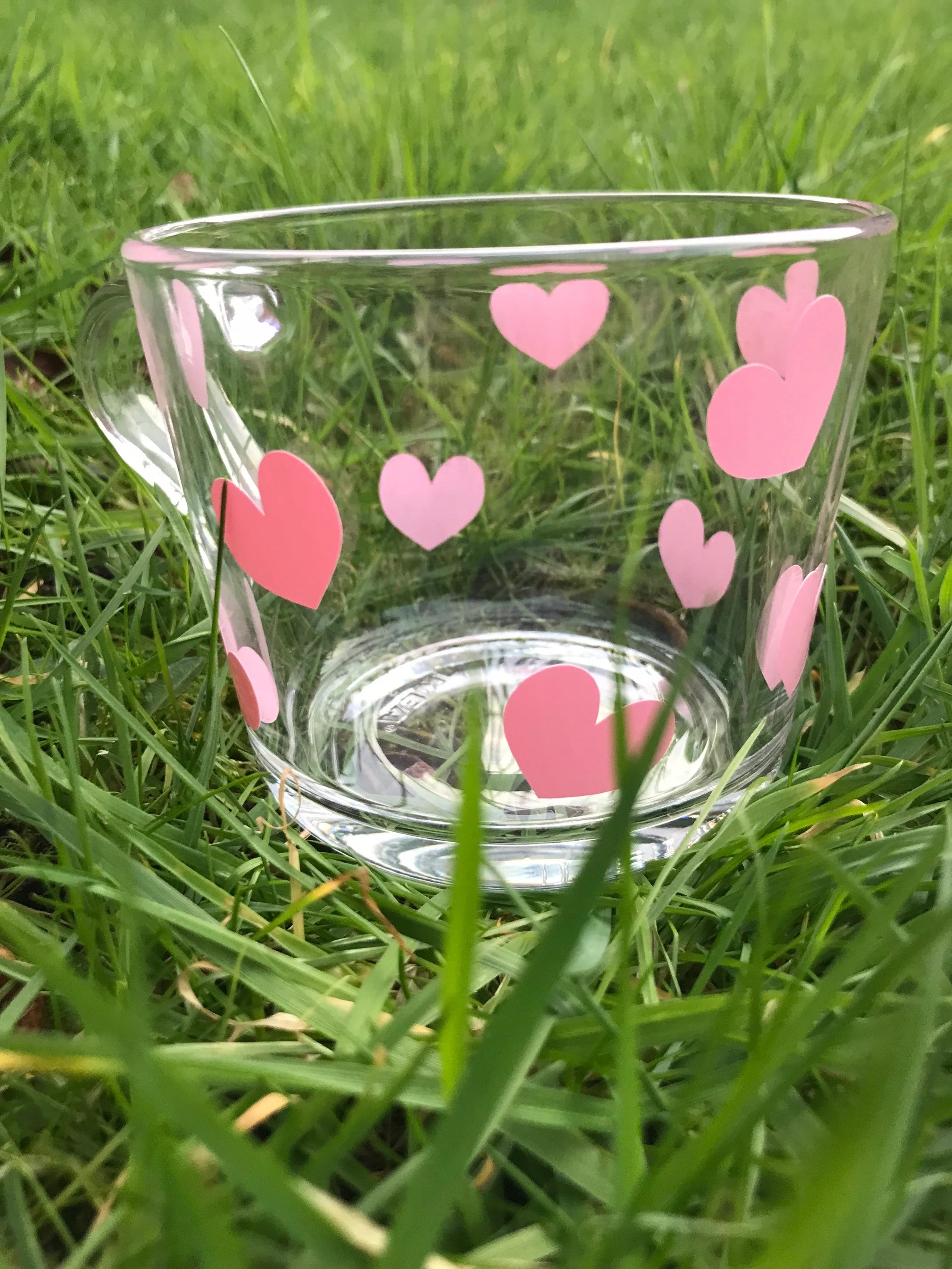 Clear glass mug with pink heart designs on a grass background