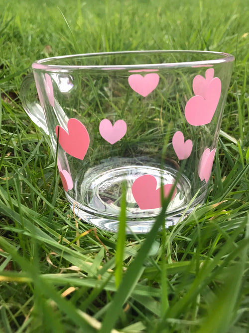 Clear glass mug with pink heart designs on a grass background