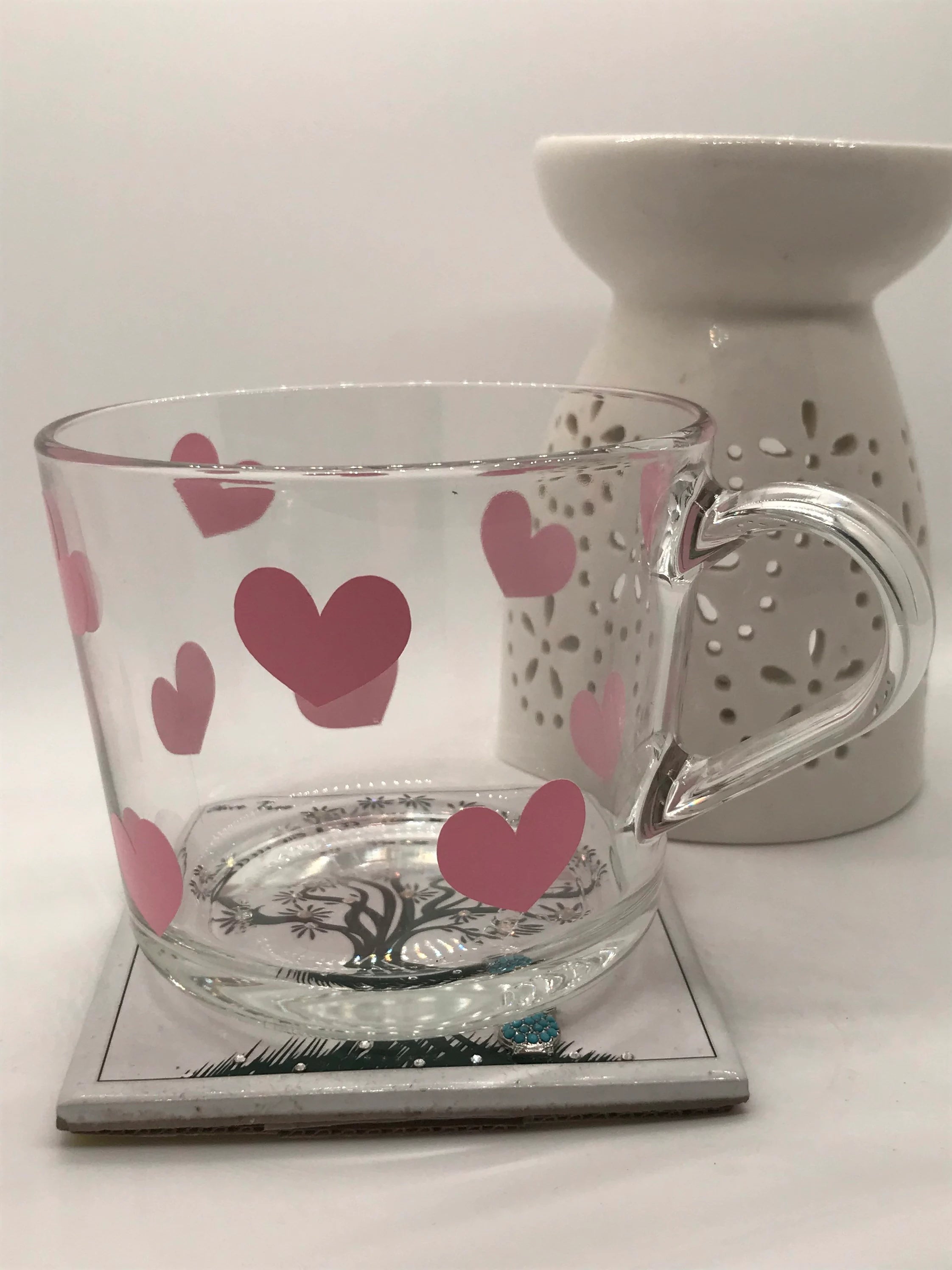 Clear glass mug with pink hearts and white ceramic warmer on a white surface