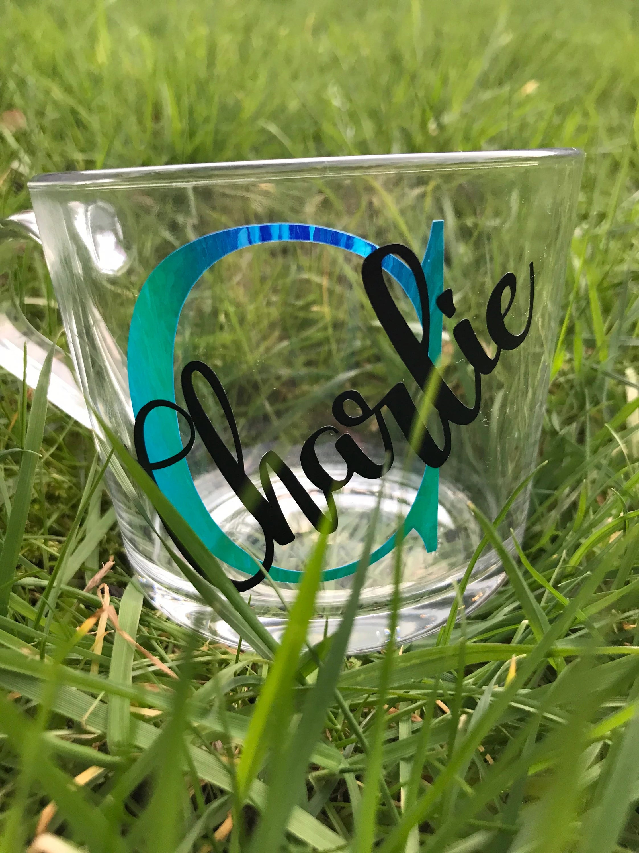 Clear glass mug with 'Charlie' and a blue initial on grass