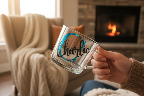 Person holding a clear mug with 'Charlie' written on it in a cozy living room with a fireplace.