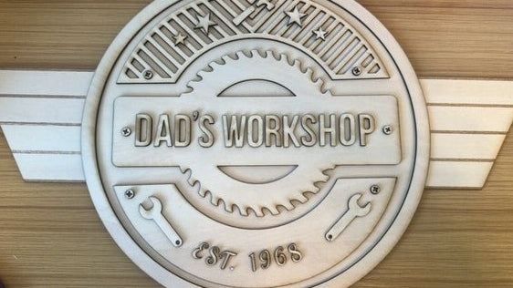 Decorative plaque with 'Dad's Workshop' text on a wooden background