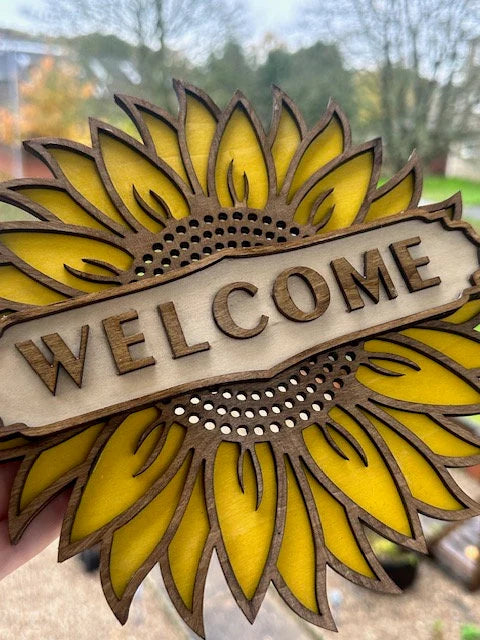 Decorative sunflower-shaped sign with 'WELCOME' text, held outdoors.