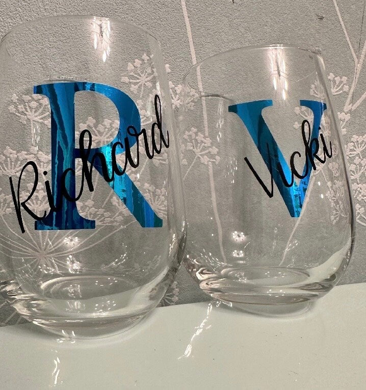 Two clear stemless glasses with blue and black lettering on