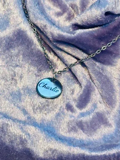 Necklace with a round pendant labeled 'Charlie' on a textured fabric background