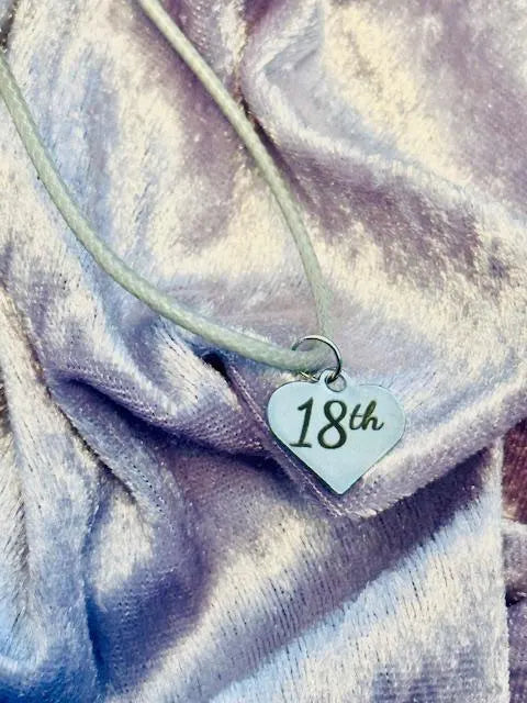 Necklace with a heart-shaped '18th' charm on a textured fabric background