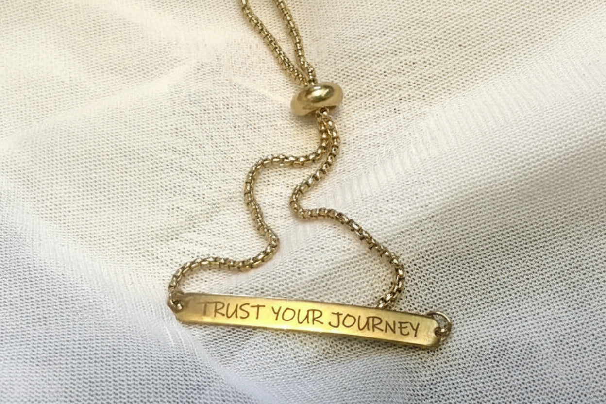 Gold stainless steel bracelet with 'Trust Your Journey' engraving on a light fabric background