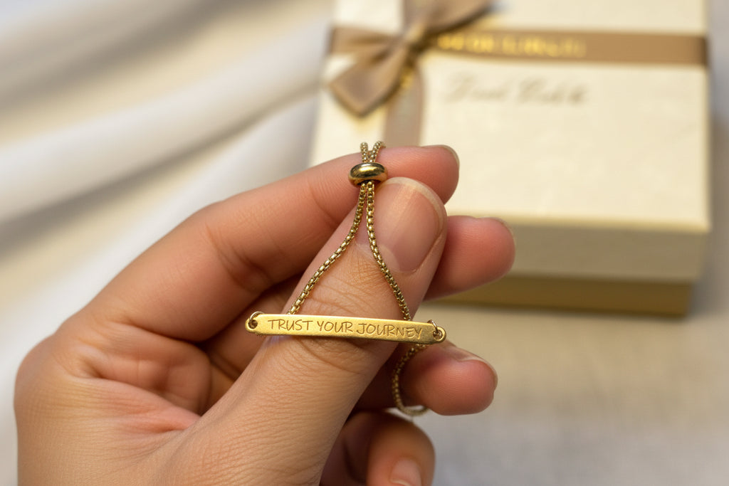 Gold stainless steel bracelet with 'Trust Your Journey' engraving on a light fabric background
