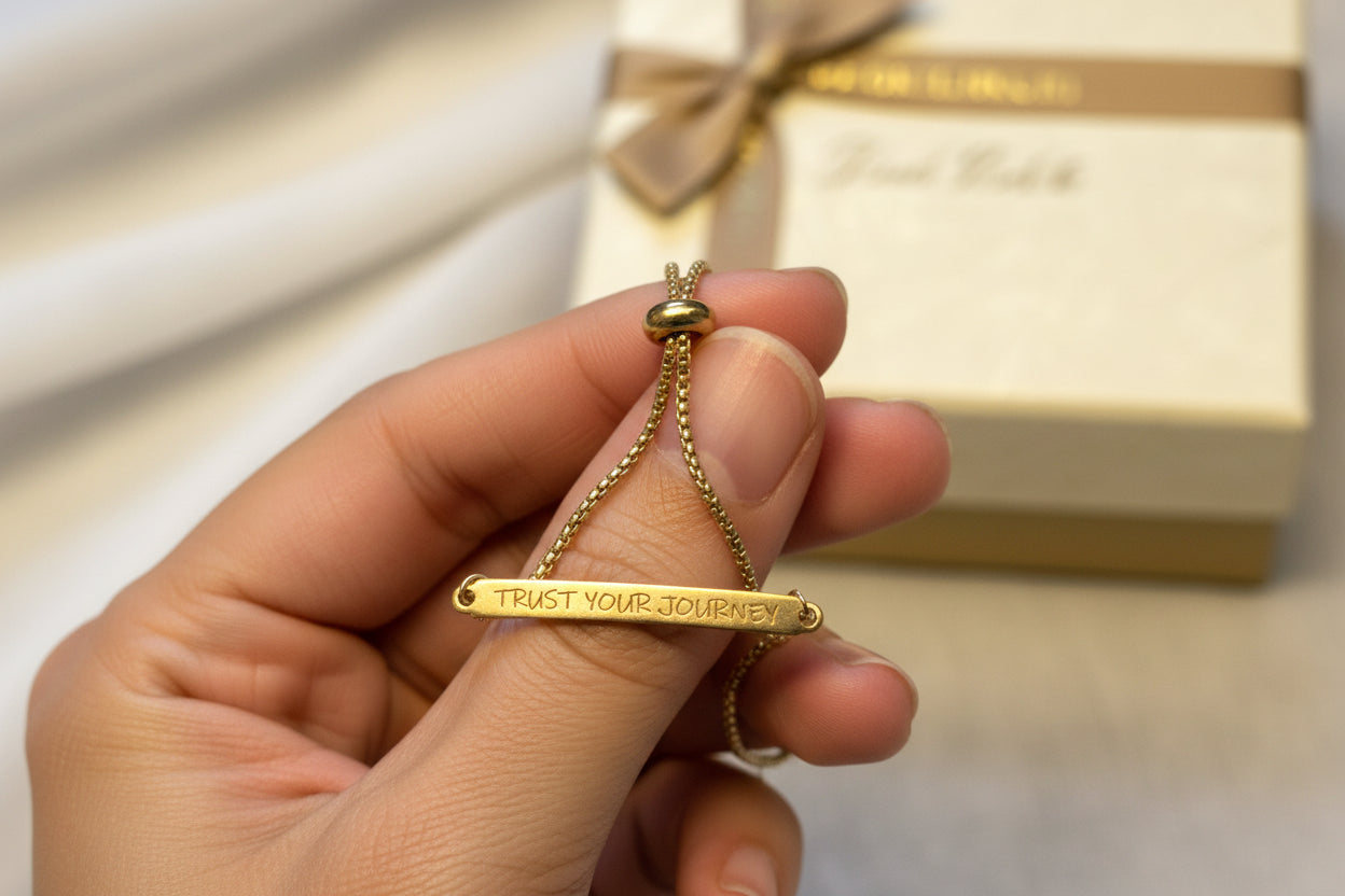 Gold stainless steel bracelet with 'Trust Your Journey' engraving on a light fabric background