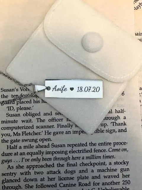 Engraved necklace with a tag reading 'Aoife heart 18.07.20' on a book page background