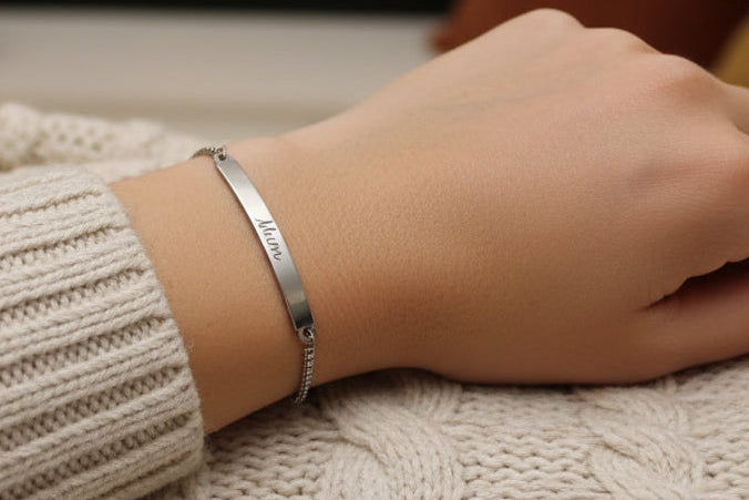 Stainless Steel bracelet with engraved text on a person's wrist wearing a beige sweater.